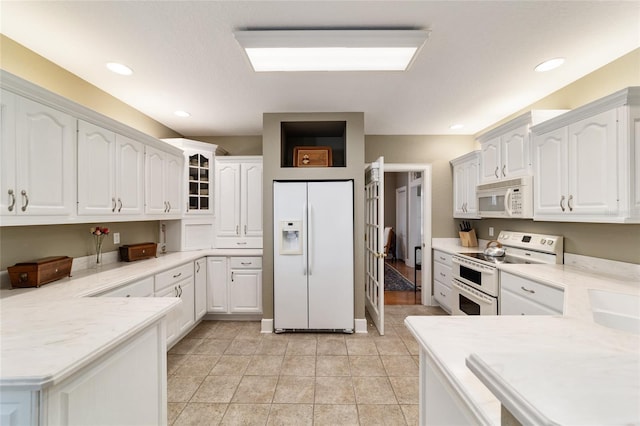 kitchen featuring a peninsula, white appliances, white cabinetry, and light countertops