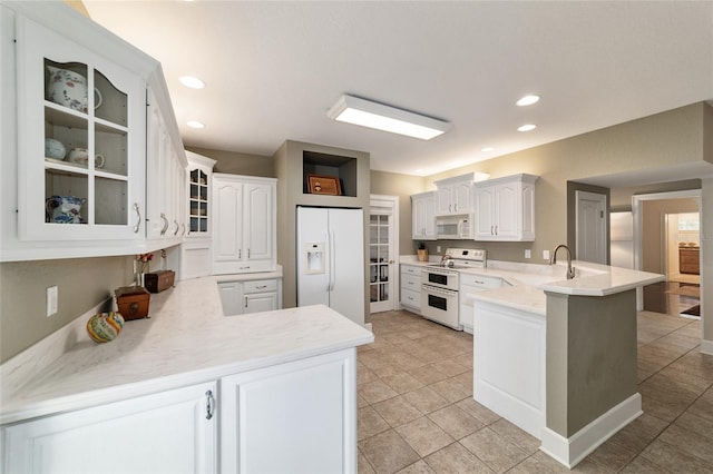 kitchen featuring white appliances, glass insert cabinets, a peninsula, light countertops, and a sink