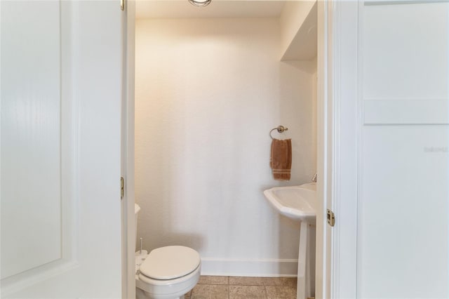 half bathroom with toilet, baseboards, a sink, and tile patterned floors