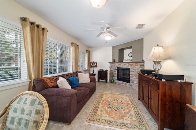 living room with light tile patterned floors, visible vents, a ceiling fan, and a stone fireplace