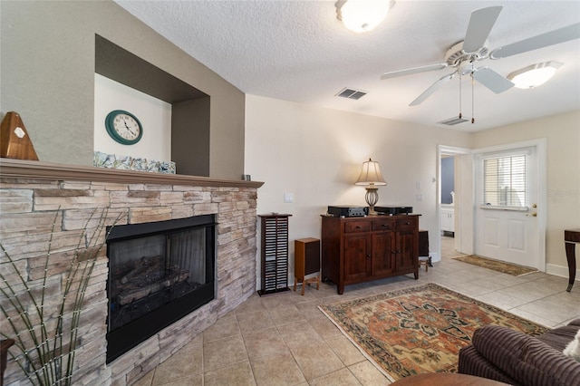 tiled living room featuring a textured ceiling, ceiling fan, a fireplace, and visible vents