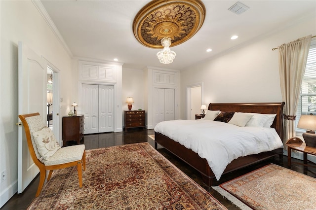 bedroom with recessed lighting, visible vents, ornamental molding, dark wood-style floors, and two closets