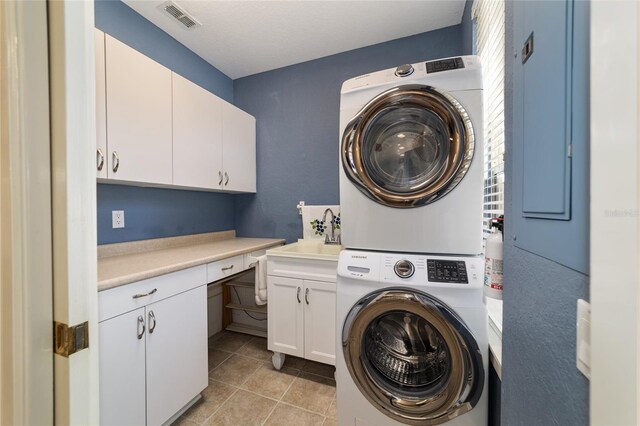 laundry room featuring cabinet space, visible vents, stacked washer / drying machine, a sink, and light tile patterned flooring