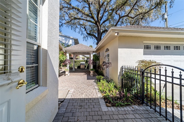 view of side of property featuring a gazebo, roof with shingles, fence, and stucco siding