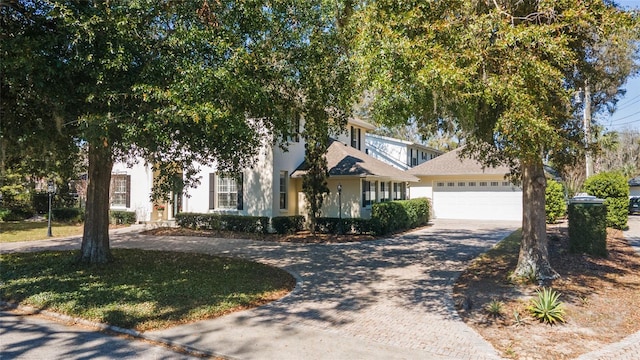 obstructed view of property featuring a front lawn, decorative driveway, an attached garage, and stucco siding