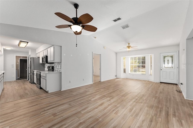 unfurnished living room featuring vaulted ceiling, light wood finished floors, and visible vents