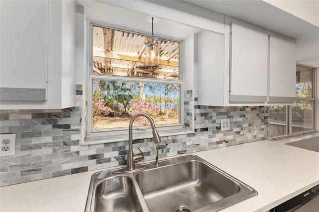 kitchen with pendant lighting, tasteful backsplash, light countertops, white cabinetry, and a sink