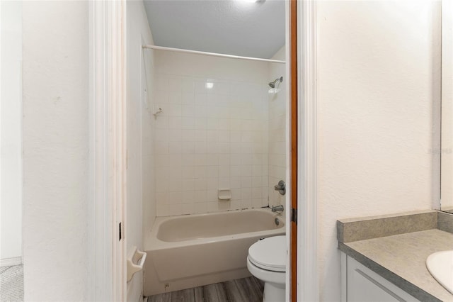 full bathroom with a textured wall, toilet, wood finished floors, vanity, and shower / bathing tub combination