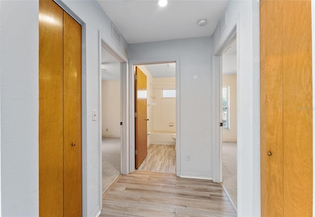 corridor with light colored carpet, visible vents, and light wood-style flooring