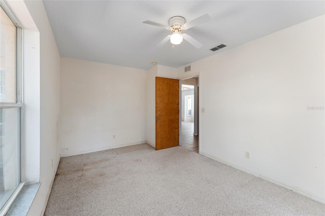 spare room featuring baseboards, visible vents, a ceiling fan, and light colored carpet