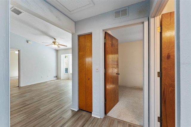 hall featuring light wood-style flooring, visible vents, and baseboards