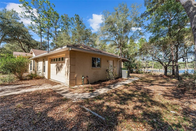 view of side of property featuring a garage, stucco siding, dirt driveway, and central air condition unit