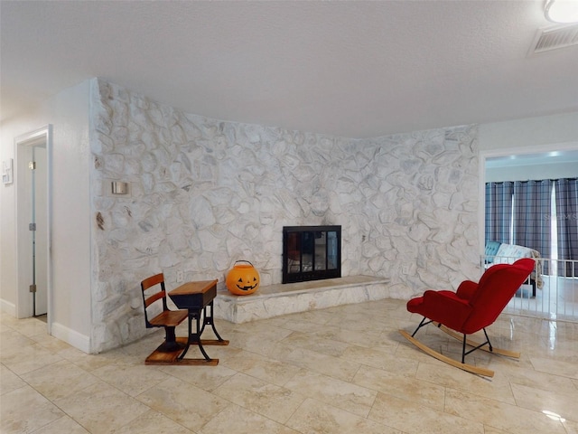 sitting room with a textured ceiling, a fireplace, visible vents, and baseboards