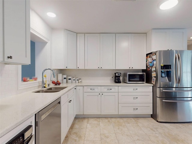 kitchen with appliances with stainless steel finishes, white cabinetry, a sink, and light stone countertops