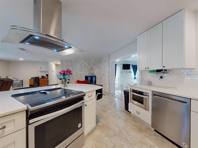 kitchen featuring island range hood, white cabinets, decorative backsplash, stainless steel appliances, and light countertops