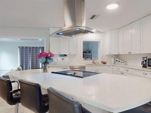 kitchen featuring tasteful backsplash, a breakfast bar, island exhaust hood, and white cabinets