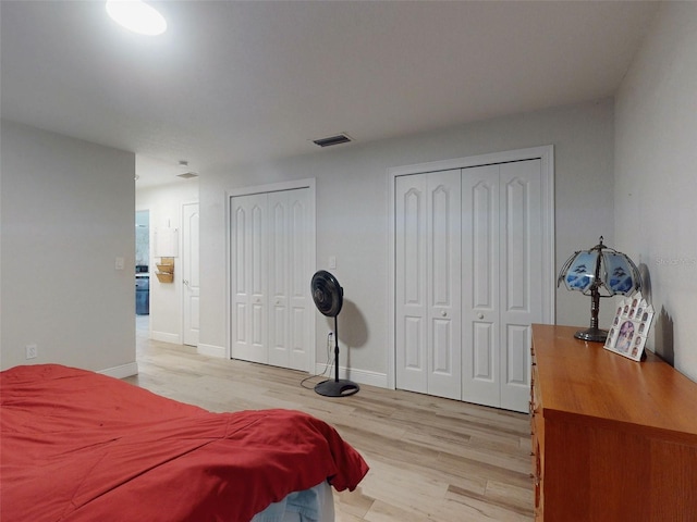 bedroom with light wood-style floors, baseboards, visible vents, and two closets