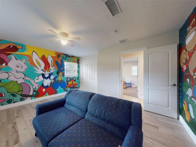 living area featuring baseboards, visible vents, a ceiling fan, light wood-style flooring, and a textured ceiling