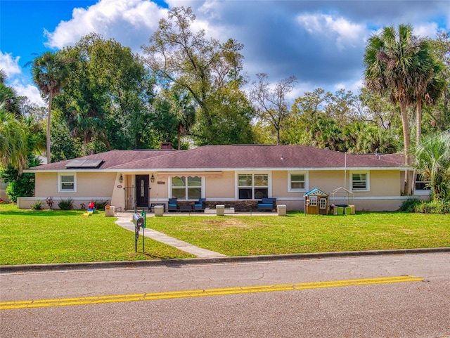 single story home featuring a front lawn, solar panels, and stucco siding