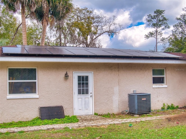 back of property featuring central AC unit, solar panels, and stucco siding