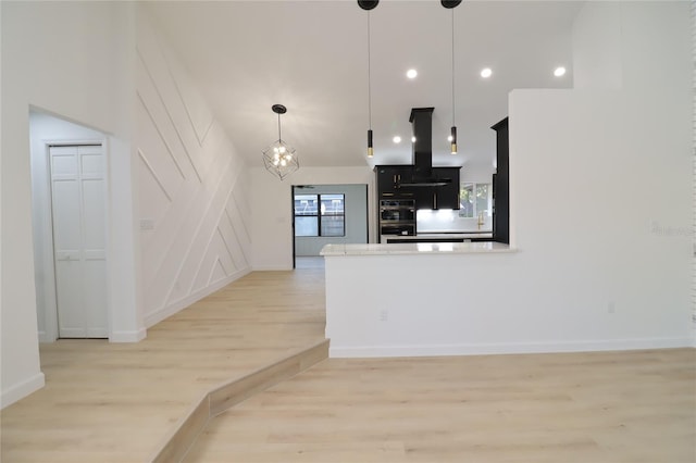 kitchen with island range hood, double wall oven, light countertops, light wood-type flooring, and pendant lighting