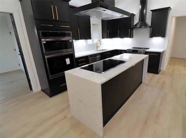 kitchen with dark cabinets, a sink, wall chimney range hood, a center island, and island exhaust hood