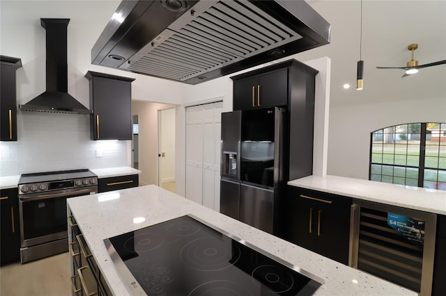 kitchen featuring dark cabinets, beverage cooler, stainless steel appliances, wall chimney range hood, and pendant lighting