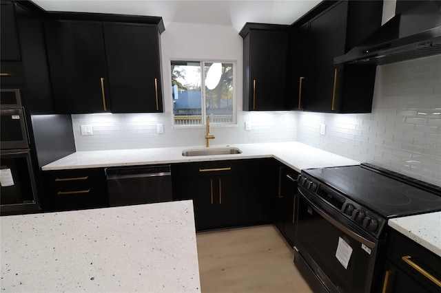 kitchen featuring decorative backsplash, wall chimney range hood, light stone countertops, black appliances, and a sink