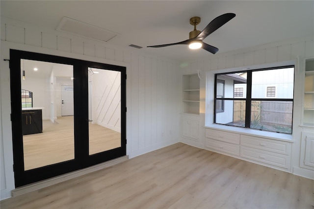 empty room with light wood finished floors, ceiling fan, built in shelves, and visible vents