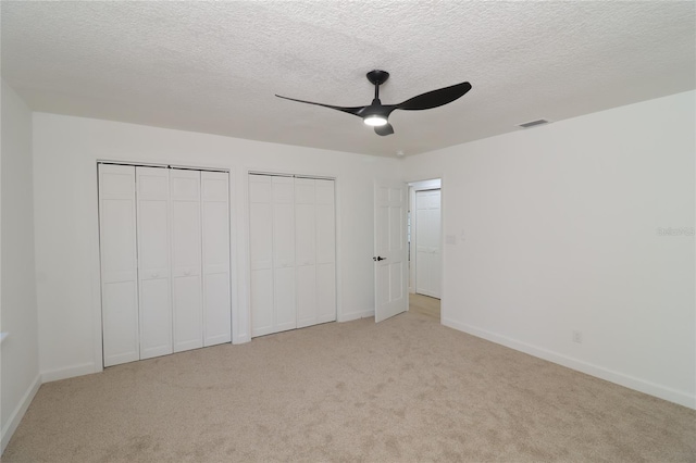 unfurnished bedroom featuring light carpet, visible vents, baseboards, a textured ceiling, and two closets