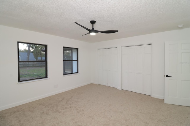 unfurnished bedroom featuring two closets, light colored carpet, a ceiling fan, a textured ceiling, and baseboards