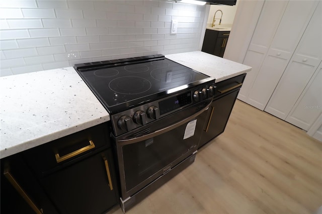 kitchen with light wood finished floors, tasteful backsplash, black electric range oven, white cabinetry, and light stone countertops