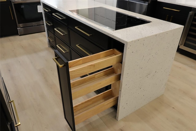 interior space with black electric stovetop, light stone counters, dark cabinets, beverage cooler, and light wood finished floors