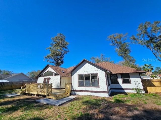 back of property with a deck, a yard, and fence