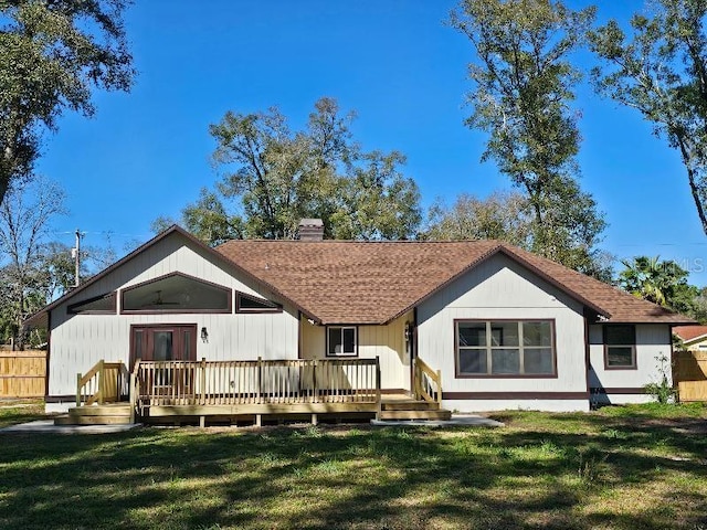 back of property featuring a shingled roof, a chimney, a lawn, and a deck