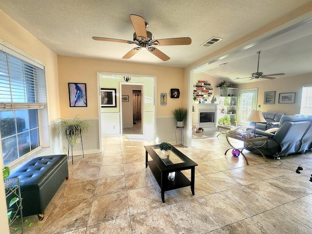 living room featuring a textured ceiling, a fireplace, visible vents, and a ceiling fan