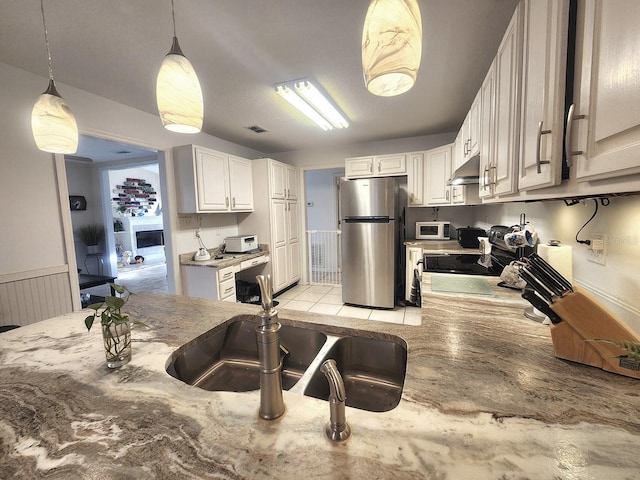 kitchen featuring white microwave, under cabinet range hood, white cabinets, freestanding refrigerator, and pendant lighting