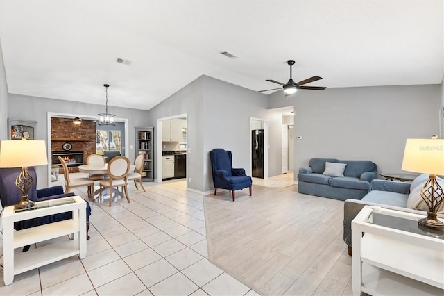 living room featuring lofted ceiling, a fireplace, visible vents, and ceiling fan with notable chandelier