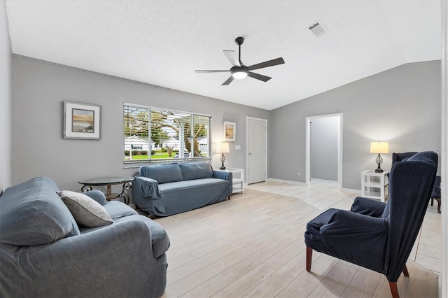 living area featuring a ceiling fan, lofted ceiling, visible vents, and a textured ceiling