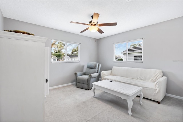 living area with a ceiling fan, light colored carpet, a textured ceiling, and baseboards