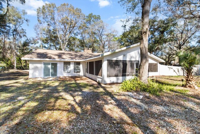 rear view of property featuring a yard, a chimney, fence, and a sunroom