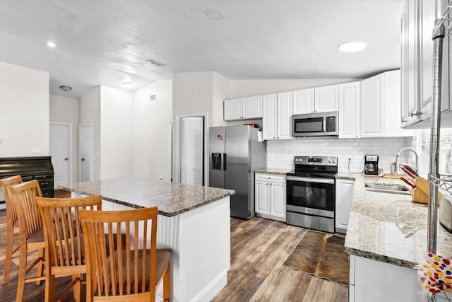 kitchen with stainless steel appliances, a sink, white cabinets, dark stone counters, and a kitchen bar