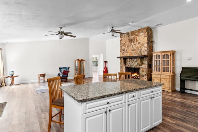 kitchen featuring a stone fireplace, dark wood-style flooring, white cabinets, open floor plan, and dark stone counters