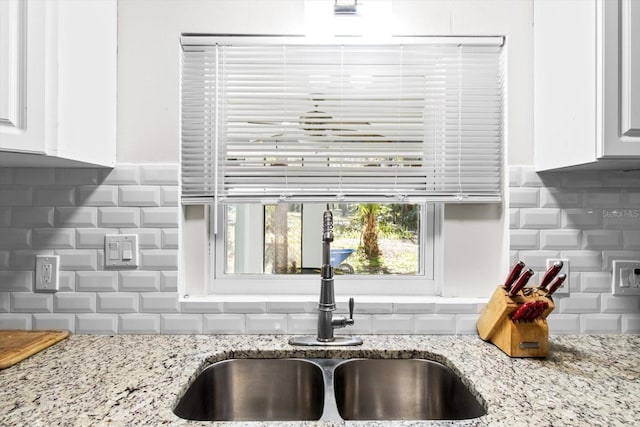 kitchen with decorative backsplash, a sink, light stone countertops, and white cabinets