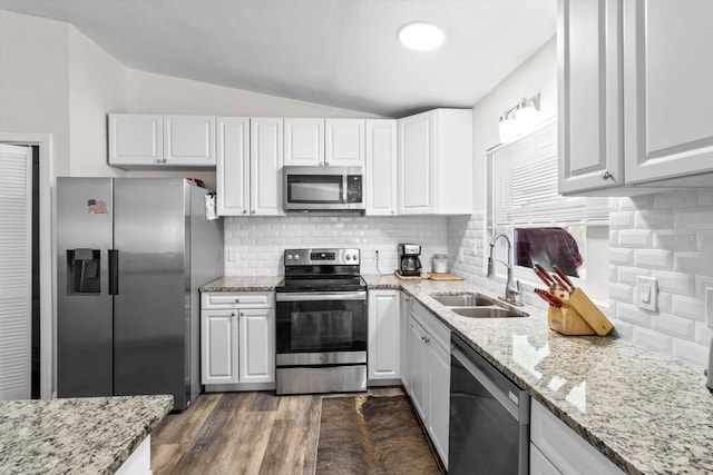 kitchen featuring stainless steel appliances, vaulted ceiling, white cabinetry, and a sink