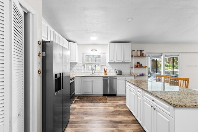 kitchen with light stone counters, stainless steel appliances, a sink, white cabinets, and dark wood finished floors