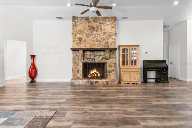 living area with a stone fireplace, wood finished floors, visible vents, and a ceiling fan