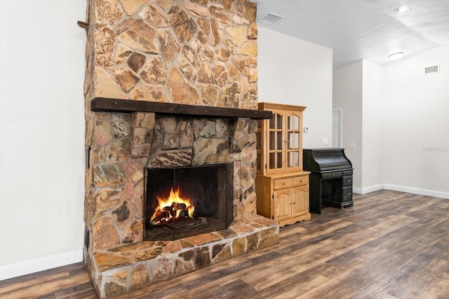 living area with a stone fireplace, dark wood-type flooring, visible vents, and baseboards