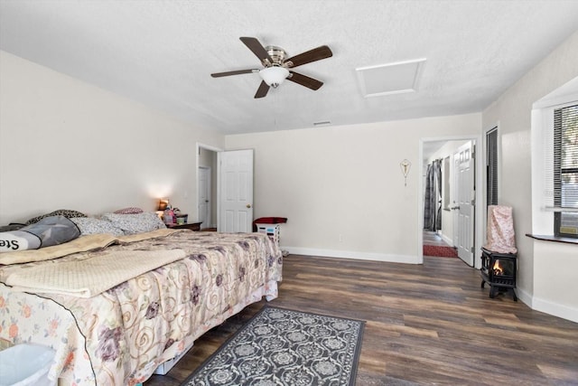 bedroom featuring attic access, baseboards, dark wood-style flooring, a wood stove, and a textured ceiling