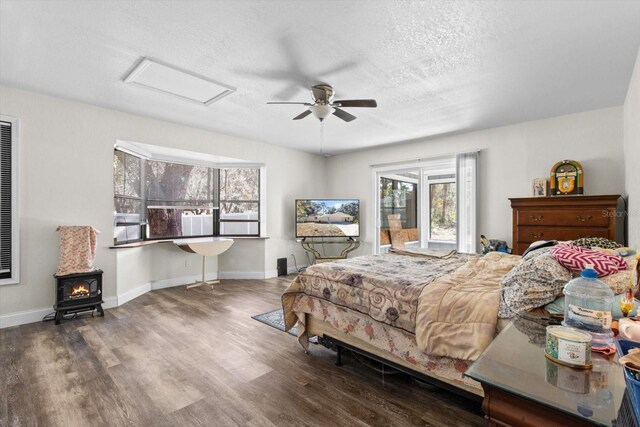 bedroom featuring attic access, a wood stove, a textured ceiling, and wood finished floors